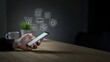 © Nishat - Person using a smartphone for online shopping with digital icons in a dark room
