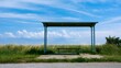© Thares2020 - A modern bus stop shelter with a bench sits under a clear blue sky in an outdoor public setting