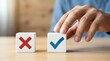 © alex - Hand choosing blue checkmark over red cross on white blocks for decision making and quality assessment