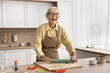 © fizkes - Happy retired woman wear eyeglasses and apron preparing dessert alone in modern kitchen, laughing, enjoy cooking time, flattening dough, making sweet cookies on holiday for family. Recipe, culinary