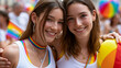 © Nick Freund - Zwei junge lächelnde Frauen umarmen sich mit Regenbogenfahne auf Stadtveranstaltung