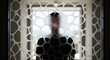 © Platon - Blurred silhouette of a person standing behind a glass screen with a modern decorative organic mesh pattern, with only one eye visible through a hole