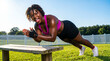 © Tatiana - Young Black woman doing pushups on a bench in a vibrant outdoor setting