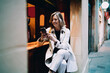 © BullRun - Smiling lady interacting with mobile device while sitting in coffee shop, adult female using smartphone for financial transactions, authentic portrait of tech lifestyle and digital connectivity.