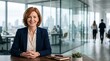 © Eve - Professional businesswoman smiling at camera, sitting at office desk in modern corporate glass office, confident executive leader portrait for business marketing and finance concepts