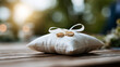 © Kateryna - A wide shot of a calm ring pillow holding softly bright wedding bands at an outdoor ceremony ring pillow faceless still softly defocused backdrop bright outdoors daylight