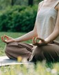 © Artem - Outdoor Meditation Practice in Peaceful Green Nature. A person sits cross-legged outdoors, practicing yoga meditation with relaxed hands in a calm green garden setting.