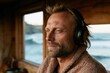 © Iryna - Middle aged man listening with headphones in seaside cabin