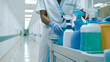 © Olga Ко - Professional healthcare janitor in uniform organizing a cleaning cart with supplies in a bright sterile clinic corridor.