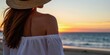 © Viktor - Woman with straw hat on beach looking at sunset over ocean. Female wears white off-shoulder top enjoying summer dusk by sea. Peaceful vacation scene with calm waves.