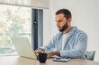 © Daniel - Young man concentrating and typing on a laptop computer, sitting at a desk in a well-lit home office, representing remote work, productivity, and modern business