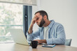 © Daniel - Stressed man gripping his forehead while looking at a laptop, feeling exhausted and frustrated by work, experiencing burnout from home office tasks