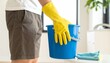 © WIVA - Person wearing yellow rubber gloves holding a blue cleaning bucket for domestic housework and home hygiene