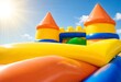 © shahjalal - Vibrant inflatable bounce house castle with slides under bright blue sky and sun, children playing, outdoor summer fun party, joyful amusement attraction recreation leisure entertainment