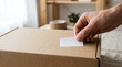 © Kinanti - Close up of hand applying adhesive sticker to cardboard parcel box
