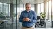 © shahinahmed - Mature businessman smiling while using a smartphone in an office