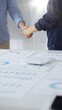 © rogerphoto - Businesspeople shaking hands over a conference table, finalizing a deal with financial documents and digital tools. Handshake concept