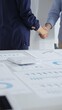 © rogerphoto - Professional businesspeople concluding deal, shaking hands near financial paperwork, calculator, pen on pristine workspace surface. Handshake concept