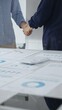 © rogerphoto - Business partners shaking hands after successful meeting, with financial documents, calculator, pen, and tablet on the table, symbolizing agreement and partnership. Handshake concept