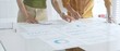 © rogerphoto - Casual business people are working together, analyzing financial data and reports using a keyboard and printed charts spread out on a table in a modern office
