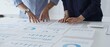 © rogerphoto - Business colleagues are examining financial reports and pointing at charts and graphs spread out on a desk, working together to analyze data and plan strategies