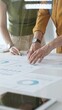 © rogerphoto - Professional team collaborating, reviewing financial documents and graphs on laptop with printed data spread across conference table in contemporary workspace. Business people concept