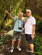 © luciano - Senior friends exploring botanical garden, man with camera pointing, showing discovery and connection with nature during active retirement leisure journey