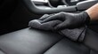 © Guzel - A person wearing a black glove cleans a black leather car interior using a microfiber cloth, professional auto detailing, car wash service, vehicle care.