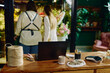 © TrueFrame Collective - Wide shot of female florist and woman discussing bouquet order in flower shop, with laptop on counter supporting retail workflow. Ideal for small business, ecommerce, service marketing