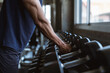 © Supachai - Close up of strong sportsman arm holding heavy dumbbell iron piece. Active male exercising power strength routine at indoor sport club fitness