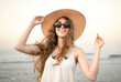 © Beatriz - Smiling young woman with windblown hair and sunglasses holding sun hat on beach, happiness, joy, positive emotions, carefree summer lifestyle and wellbeing concept