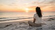 © Toni - Woman sits cross-legged on beach towel watching sunset over calm ocean waves