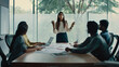 © cjsolanop - Young woman leads team in bright modern meeting room. Hands gesturing, she explains project with confidence and energy. Colleagues listen attentively, some taking notes or using laptops