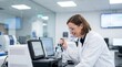 © Sopha - Smiling female researcher working with scientific equipment and data analysis screens in a bright medical lab.
