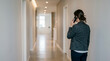 © DNA STUDIO - A person dressed in business casual attire walks while talking on a mobile phone in a bright, clean hallway.