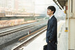 © One - 駅のホームで電車を待つ20代男性ビジネスマン