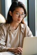 © TE - Concentrated asian woman using laptop in contemporary office filled with natural light and a productive atmosphere