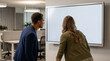 © Mehedi - A businesswoman and a male colleague stand before a large blank display screen in a modern open-plan office in the evening, conveying late-night business review and digital strategy.