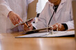 © Smallroombigdream - Healthcare professionals reviewing patient records and discussing medical documentation in a clinical office. Teamwork between doctors supports diagnosis, treatment planning