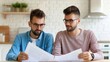 © Intelligent Horizons - A pair of men wearing glasses and casual attire sit at a dining table engrossed in reviewing papers suggesting a moment of partnership and planning in a bright contemporary home interior