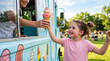 © MargoD - Excited little girl with joyful expression receiving colorful double scoop waffle cone from vendor against blue ice cream truck and sunny park backdrop