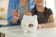 © New Africa - Woman with her daughter putting coins into piggy bank at home, selective focus