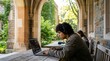 © Konstiantyn Zap - College student studying outdoors with laptop and headphones at campus archway for remote study and academic background