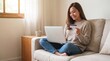 © Stephanie - Asian woman shopping online with card and laptop on sofa