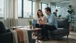 © Marc - A couple is sitting on a sofa in a modern office and looking at a mobile phone.