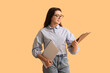 © Pixel-Shot - Young beautiful businesswoman holding laptop and clipboard on yellow background