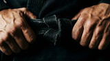 Close-up of hands tightening a worn black belt knot on a dark martial arts gi