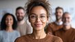© StockAlchemy - Smiling businesswoman with colleagues in the background looking at the camera