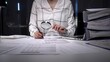 © Hanna - Professional woman uses magnifying glass and pen to scrutinize financial reports and documents on an office desk, symbolizing auditing, investigation and detailed data analysis