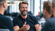 © Katerina Bond - A smiling middle-aged man gestures while discussing ideas with colleagues in a modern office meeting.